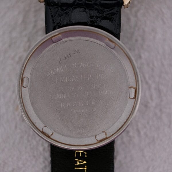 Close-up of the back of a Hamilton Accumatic III Cal. 672 wristwatch shows Hamilton Watch Co, Lancaster, PA, 10K RGP Bezel, Stainless Steel Back, R 66163, 639T-6 inscribed. The watch features a black leather strap.