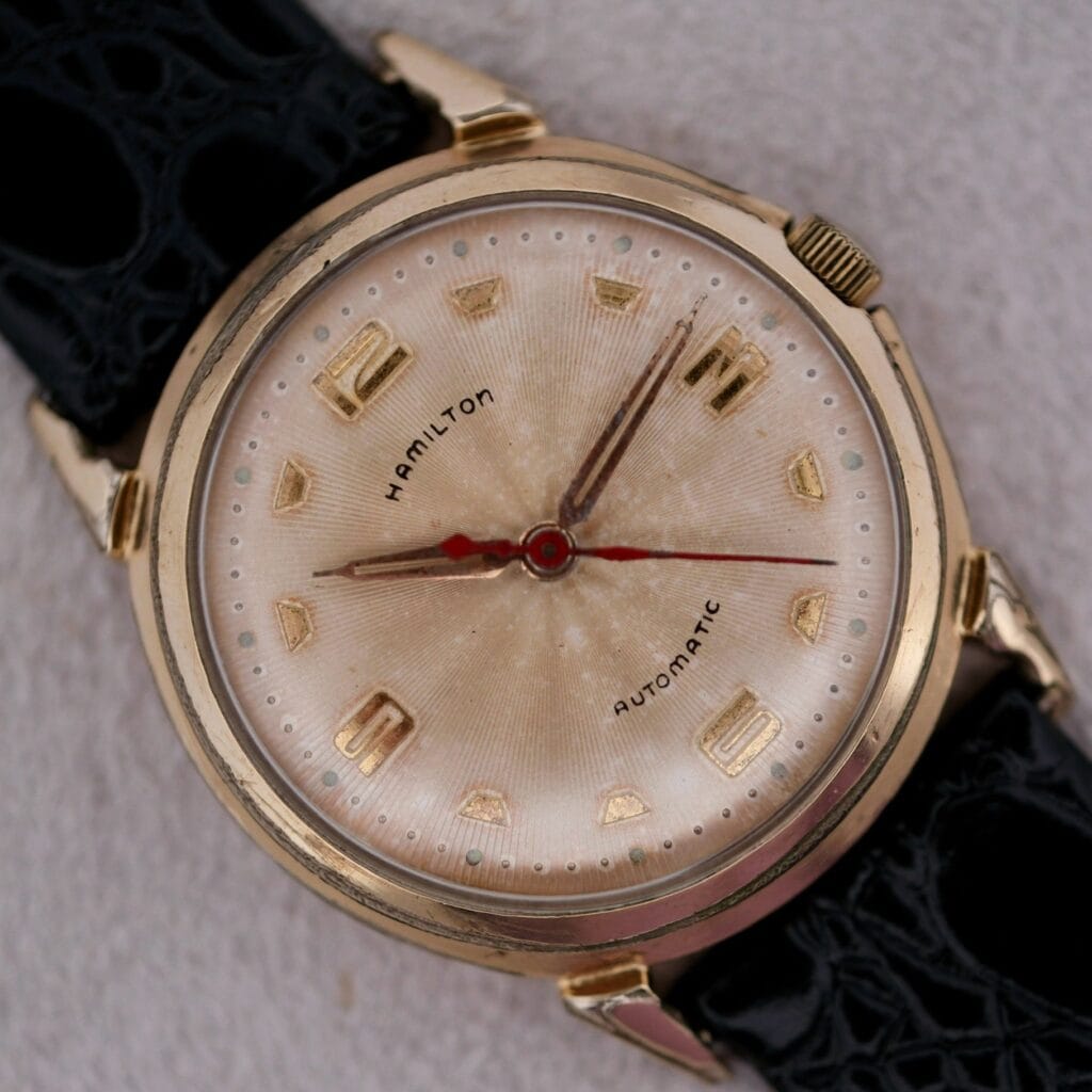 The Hamilton Accumatic III Cal. 672 is a vintage gold wristwatch featuring a textured cream dial and classic black leather strap.