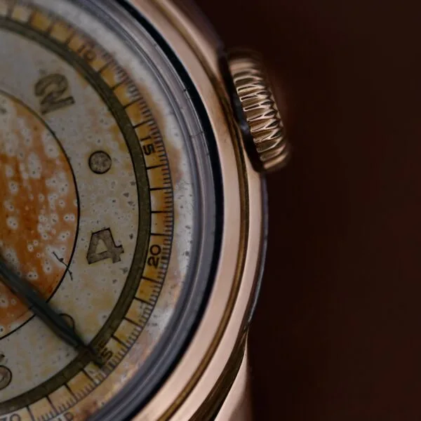 Close-up of a 1945 Movado Military Dial with noticeable wear and patina. The dial features numerals and markers, complemented by a prominent winding crown on the right. A textured, aged look adorns the metallic 14k gold bezel of this Cal. 470 timepiece.