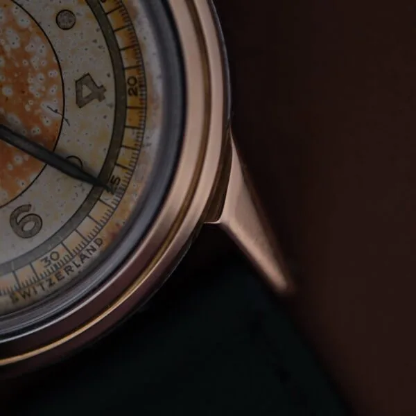 Close-up of a vintage 1945 Movado Military Dial watch featuring a darkened dial. It has a round metal case with visible hour markers and numbers 1-4 and part of 5. The text Switzerland is partially visible at the bottom.