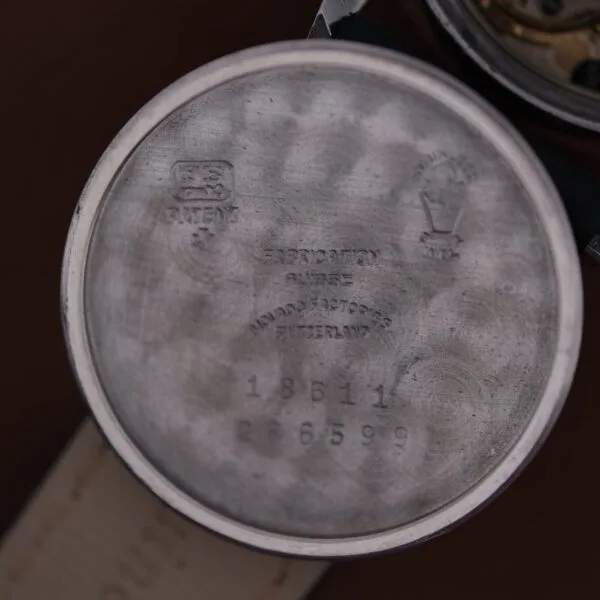 The watch case back image reveals engravings with logos, the text Fab. Suisse, Movado Factories Switzerland, serial numbers 18611 and 2665999, all on a circular brushed surface. This is from the 1945 Movado Military Dial with 14k Gold Bezel, Cal. 470.