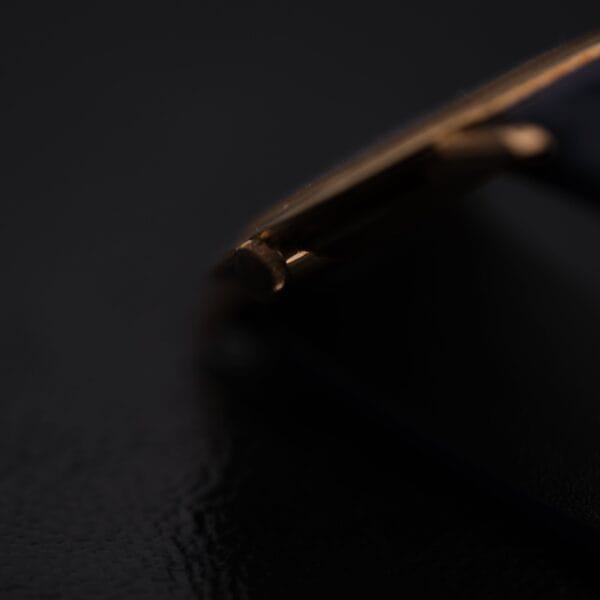 Close-up of a gold corner of an IWC International Watch Co. Mens 18k Gold Tiffany & Co. Stamp Watch against black, with lighting highlighting the metallic edge and the shadows creating a dramatic contrast.