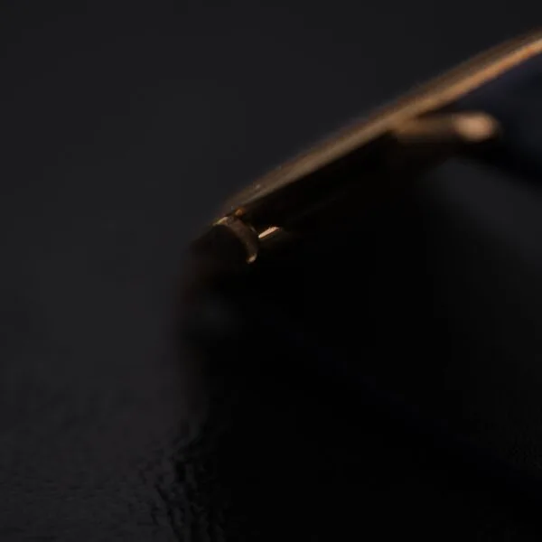 Close-up of a gold corner of an IWC International Watch Co. Mens 18k Gold Tiffany & Co. Stamp Watch against black, with lighting highlighting the metallic edge and the shadows creating a dramatic contrast.