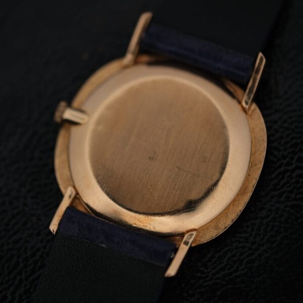 Back view of an IWC International Watch Co. mens 18k gold Tiffany & Co. stamp watch with a round case, exhibiting slight scratches and wear, and a dark leather strap attached to the case via metal lugs.