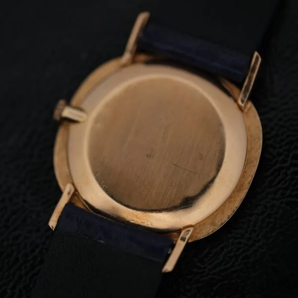 Back view of an IWC International Watch Co. mens 18k gold Tiffany & Co. stamp watch with a round case, exhibiting slight scratches and wear, and a dark leather strap attached to the case via metal lugs.