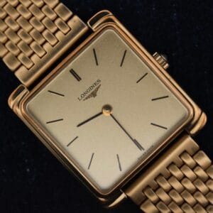 The Longines Square Case Sapphire Crown features a gold square case, gold mesh band, minimal black hour markers, and two hands on a plain gold face, showcased against a black background.