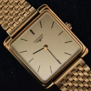 The Longines Square Case Sapphire Crown features a gold square case, gold mesh band, minimal black hour markers, and two hands on a plain gold face, showcased against a black background.