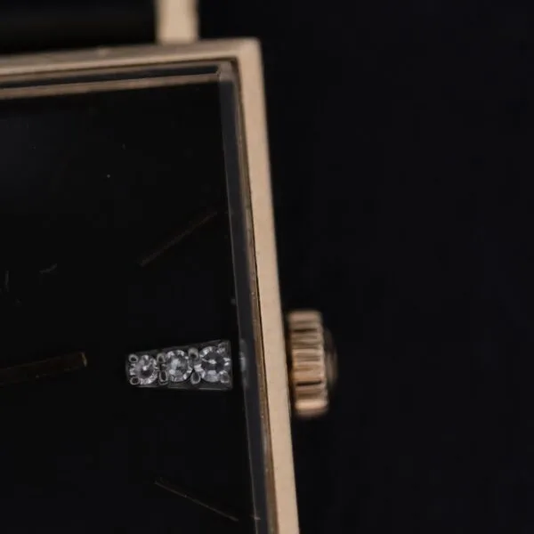 Close-up of the Omega 14K Square Case Diamond Markers showing its black watch face with minimal markings, gold-colored border, textured crown, and a silver or diamond-like hour marker.