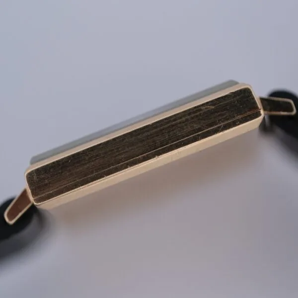 A close-up side view of the Omega 14K Square Case Diamond Markers watch, featuring a rectangular gold case with black straps against a plain, light background.