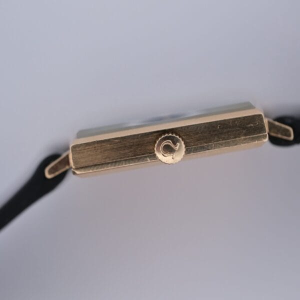 Close-up side view of the Omega 14K Square Case Diamond Markers watch with a black strap, highlighting its crown and rectangular case against a plain light background.