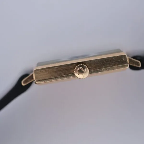 Close-up side view of the Omega 14K Square Case Diamond Markers watch with a black strap, highlighting its crown and rectangular case against a plain light background.