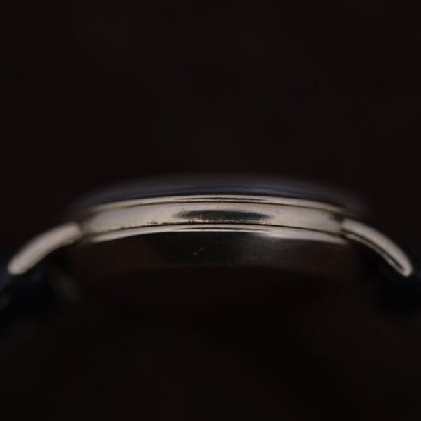 Close-up side view of the Omega Automatic Bumper Small Seconds silver case against a dark background, highlighting its curved edges and case details with strap ends partially visible.