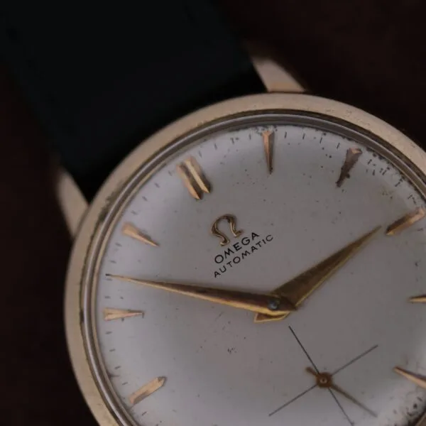 A close-up view of the Omega Automatic Bumper Small Seconds wristwatch featuring a white face, gold hour markers and hands, black strap, and visible Omega logo with Automatic on the dial.