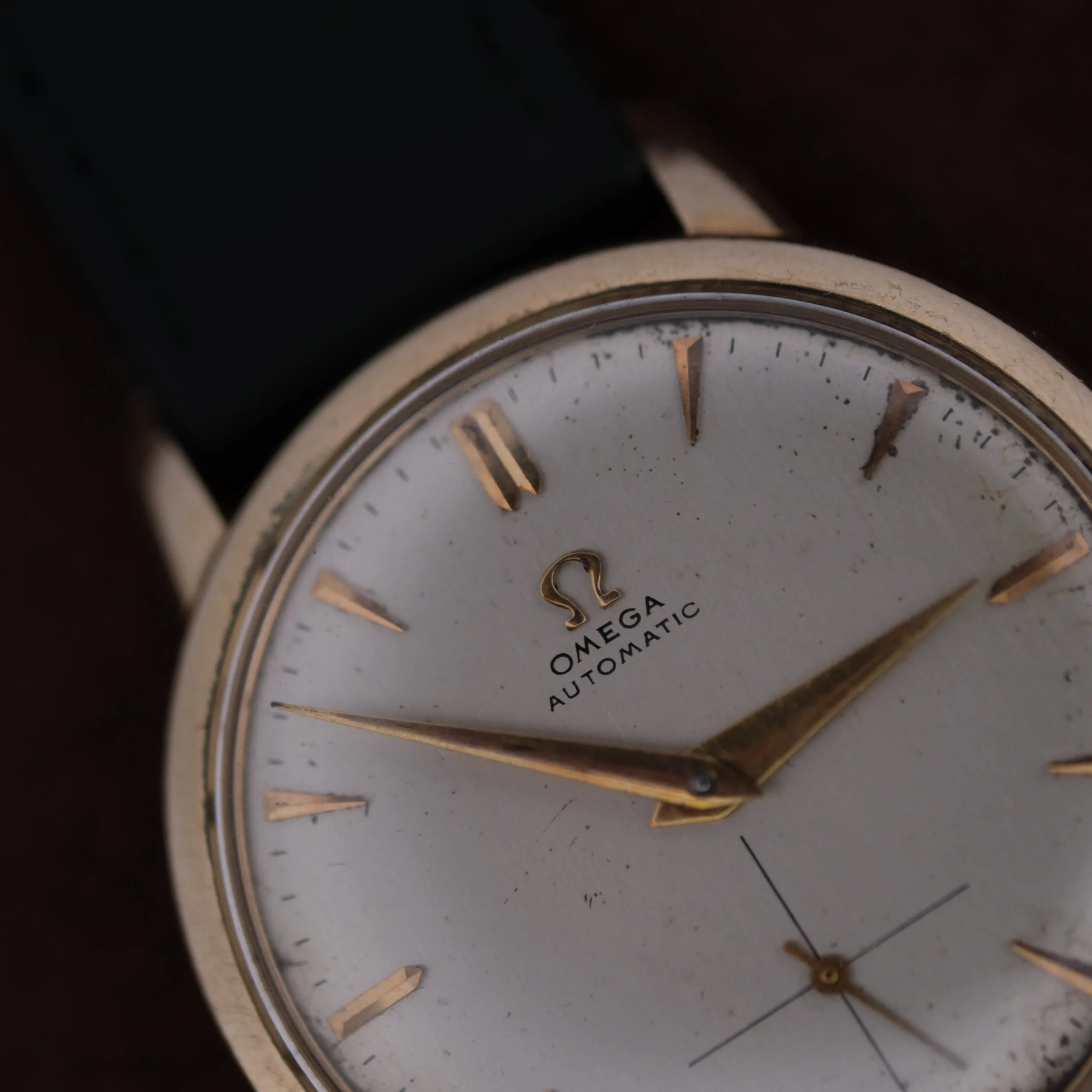 A close-up view of the Omega Automatic Bumper Small Seconds wristwatch featuring a white face, gold hour markers and hands, black strap, and visible Omega logo with Automatic on the dial.