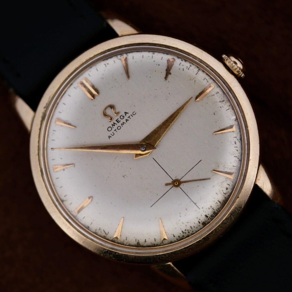 Close-up of the Omega Automatic Bumper Small Seconds wristwatch, featuring a gold case, black leather strap, and a distinctive small seconds subdial.