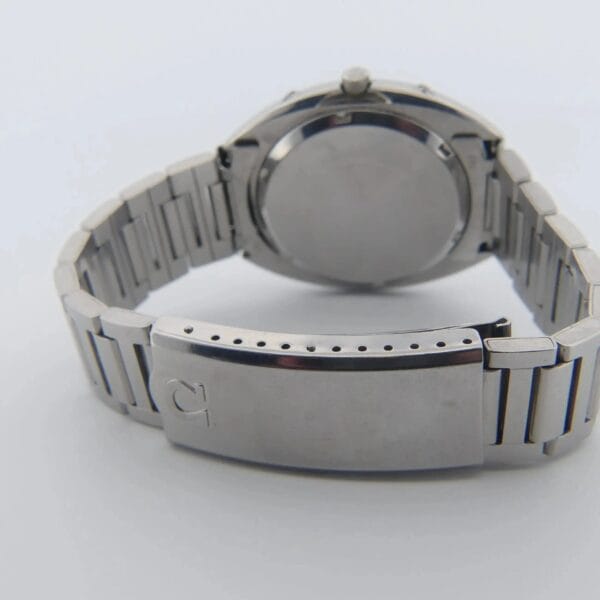 The Omega Megaquartz 32 KHz Day/Date Cal. 1310 is shown from the back, with its silver metal bracelet, closed clasp, and a plain round case back. The clasp features a small engraved letter G on the left side.