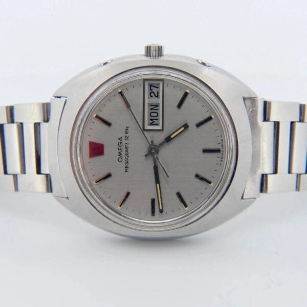 A silver Omega Megaquartz 32 KHz wristwatch with a stainless steel band, showing MON and 27 on its face. It features black hour markers and hands, with OMEGA MEGASONIC 720 Hz on the dial.