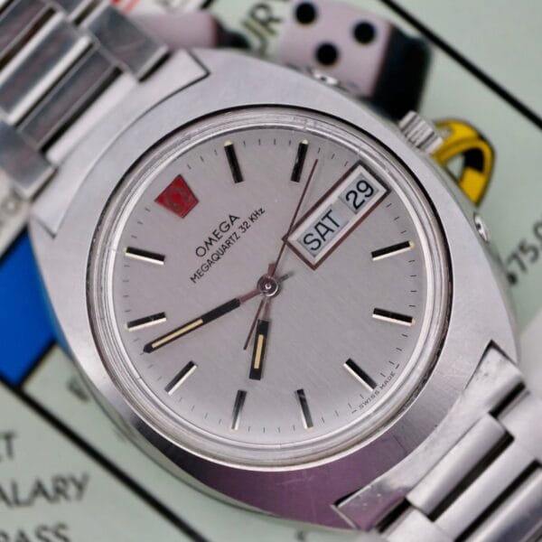 An Omega Megaquartz 32 KHz Day/Date Cal. 1310 wristwatch, showing time, day, and date, rests on a Monopoly game board.