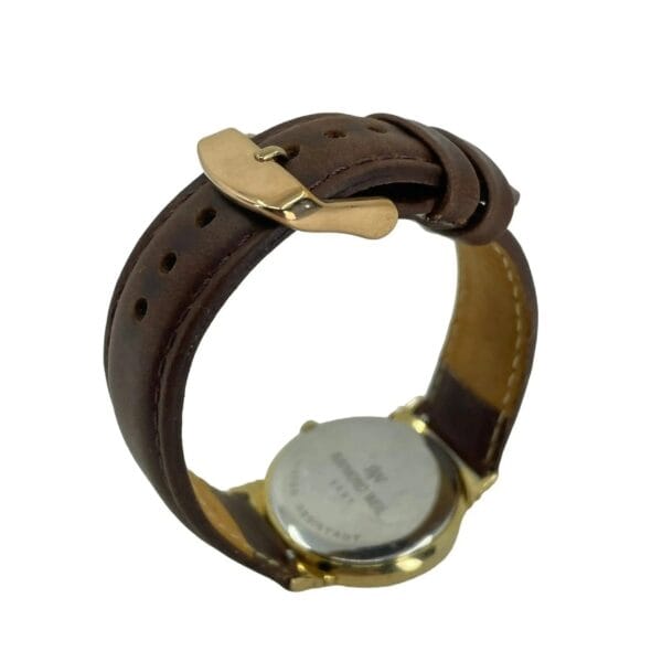 A Raymond Weil 5531 Men’s Swiss Quartz Watch is displayed with a brown leather strap and gold-tone buckle, showcasing the engraved text on the back case. The strap is fastened circularly.