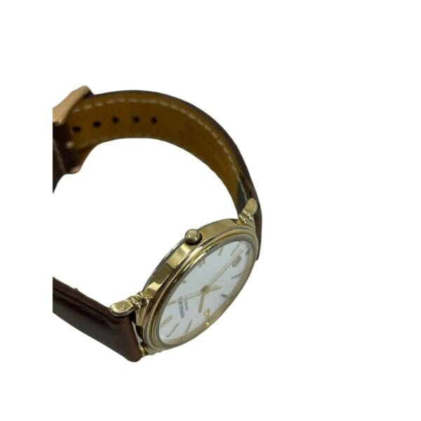 A close-up of the Raymond Weil 5531 Men’s Swiss Quartz Watch featuring a round gold-tone case, brown leather strap, and a white face with black hour markers; it has a small crown on the right side and is set against a plain white background.