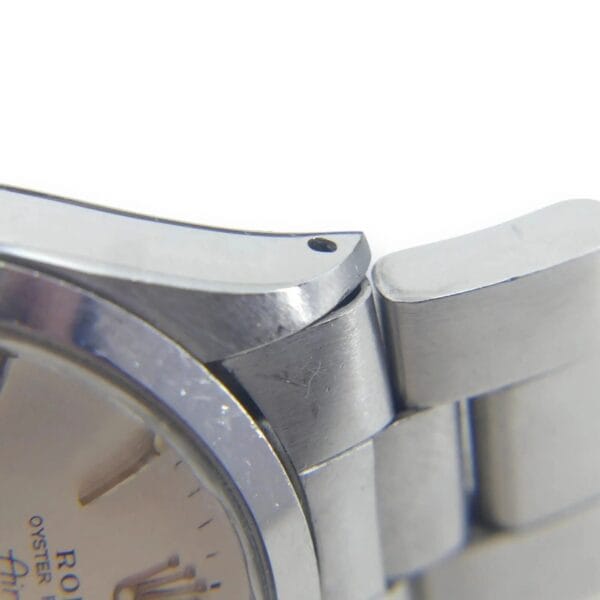Close-up of a Rolex Air King Precision Mens Stainless Steel Watch 5500, silver dial, showing the case edge, one lug, and part of the metal bracelet with minor scratches and a small hole near the lug.