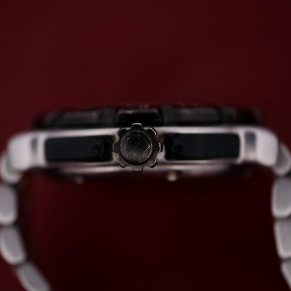 A close-up side view of the Tag Heuer Formula 1 Stainless Steel WAC 1111-1 with a metallic crown, white and black band links, set against a dark red background.