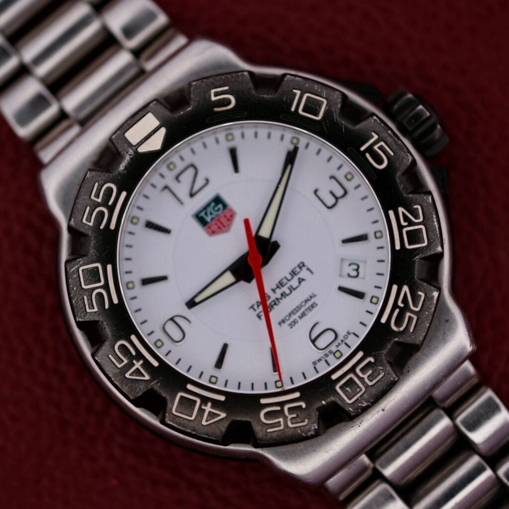 A Tag Heuer Formula 1 Stainless Steel WAC 1111-1 wristwatch with a white face and stainless steel band rests on a red textured background.