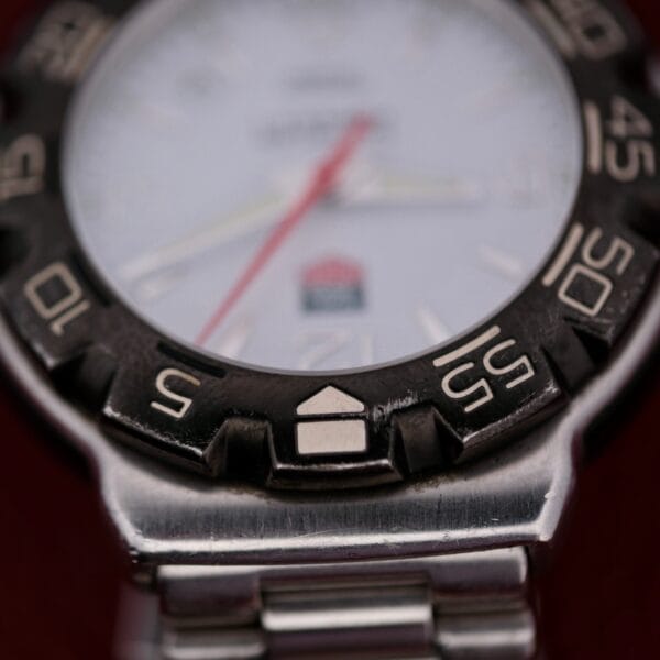 Close-up of the Tag Heuer Formula 1 Stainless Steel WAC 1111-1 wristwatch, highlighting the silver and black metal band and raised numeral bezel; watch hands and face details appear blurred in the background.