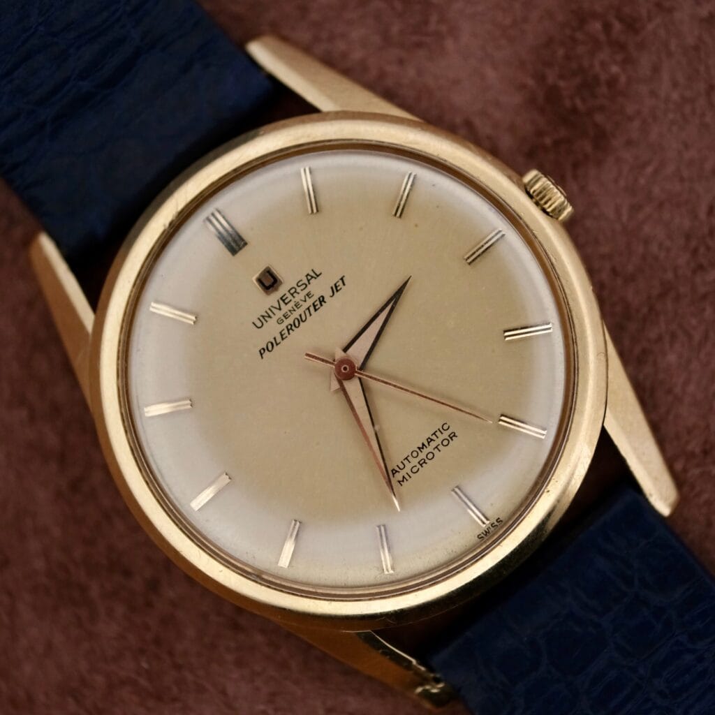 Universal Geneve Polerouter Jet 18k Cal. 215-9 with cream dial and blue leather strap, displayed on a brown surface.