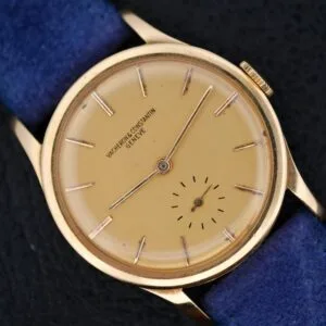 A Vacheron Constantin V453 Calatrava 18k Gold wristwatch (1950s, 34mm) featuring a round beige dial, thin hour markers, blue strap, and small seconds subdial at 6 o’clock, displayed on a black surface.