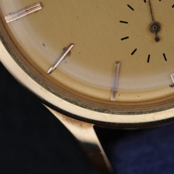 A close-up of a Vacheron Constantin V453 Calatrava 18k Gold - 1950s 34mm VC, highlighting its worn round beige dial with faded hour markers, scratched surface, and visible minute and hour hands.