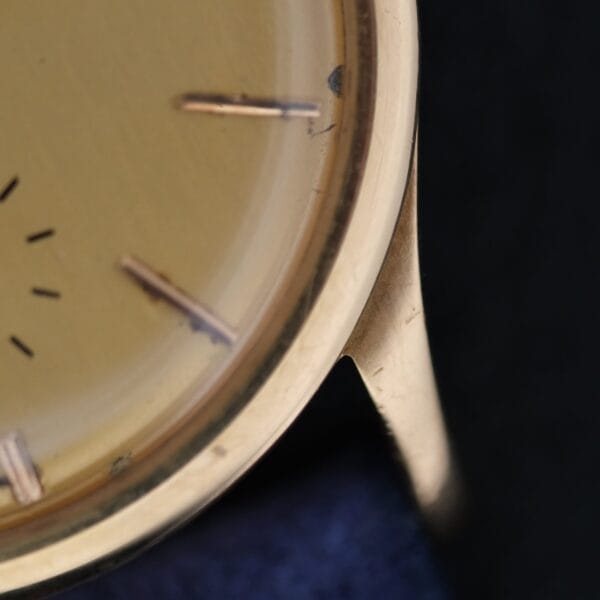 Close-up of the Vacheron Constantin V453 Calatrava 18k Gold - 1950s 34mm VC, showing part of the face, three hour markers, and the case edge against a dark, blurred background.