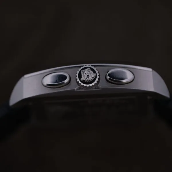 Close-up of the Versace Character Tonneau Swiss Made Chronograph’s side, featuring two round push buttons and a crown with an engraved logo, set against a dark background.