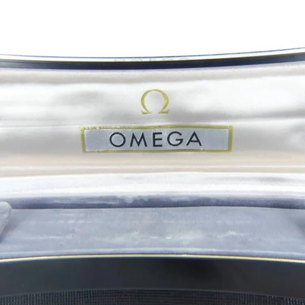 The image reveals the inside lid of a Vintage Omega Continental Can watch box, featuring a white satin lining. The Omega logo, with its iconic symbol and OMEGA text, is printed in black on the fabric within the lid.