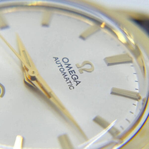 Close-up of the Vintage Omega Continental watch face, showcasing gold hands and markers. OMEGA and AUTOMATIC with the Omega logo are printed on it, while the hands point near 2 oclock.