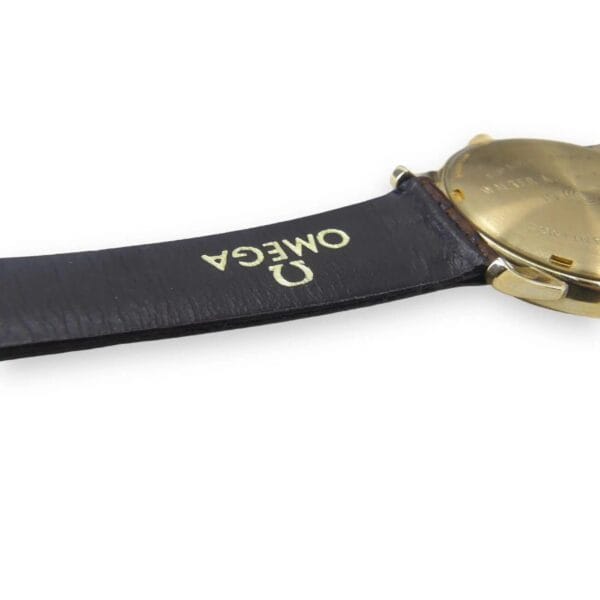 A close-up shows the back of a Vintage Omega Continental Can watch with a black leather strap embossed with OMEGA in white. The watch case looks gold.