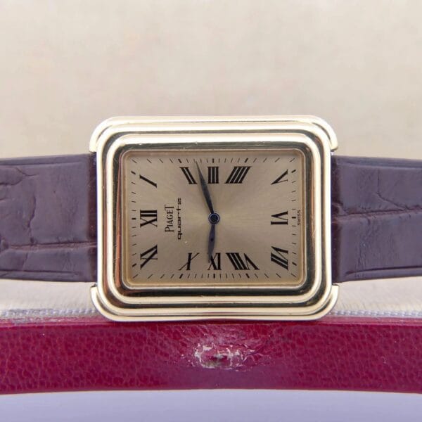 The Vintage Piaget Protocole 74121 features an 18k gold stepped rectangular case, a brown leather strap, and a watch face with Roman numerals and black hands. The Piaget brand is above the center, set against a red and beige background.