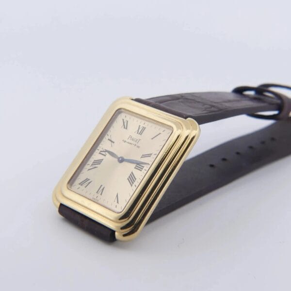The Vintage Piaget Protocole 74121 features a square 18k gold stepped case with a cream face, Roman numerals, black hands, and a black leather strap, angled on a plain surface.