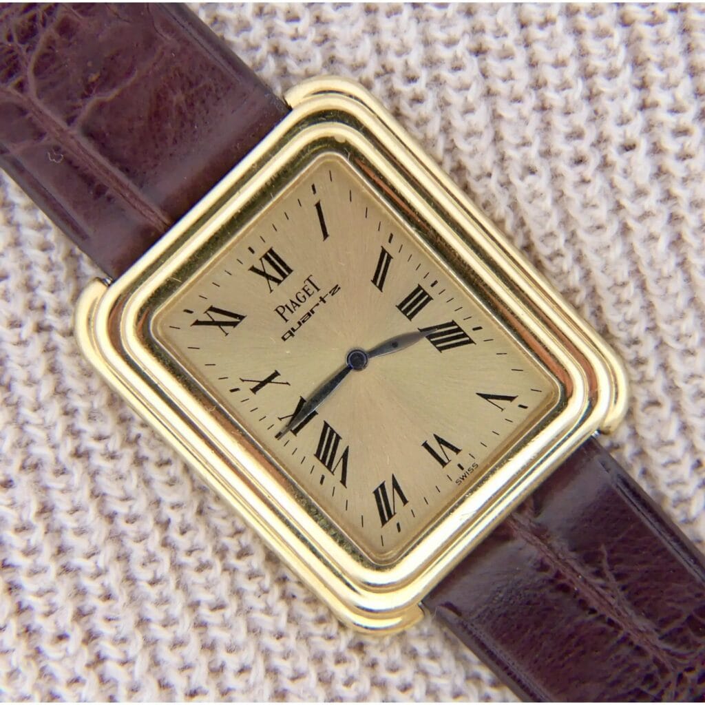 Vintage Piaget Protocole 74121 wristwatch featuring an 18k gold stepped case, Roman numerals, and a brown leather strap, elegantly displayed on textured beige fabric.