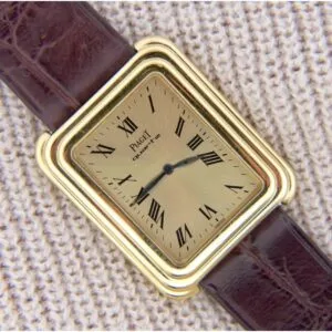 Vintage Piaget Protocole 74121 wristwatch featuring an 18k gold stepped case, Roman numerals, and a brown leather strap, elegantly displayed on textured beige fabric.