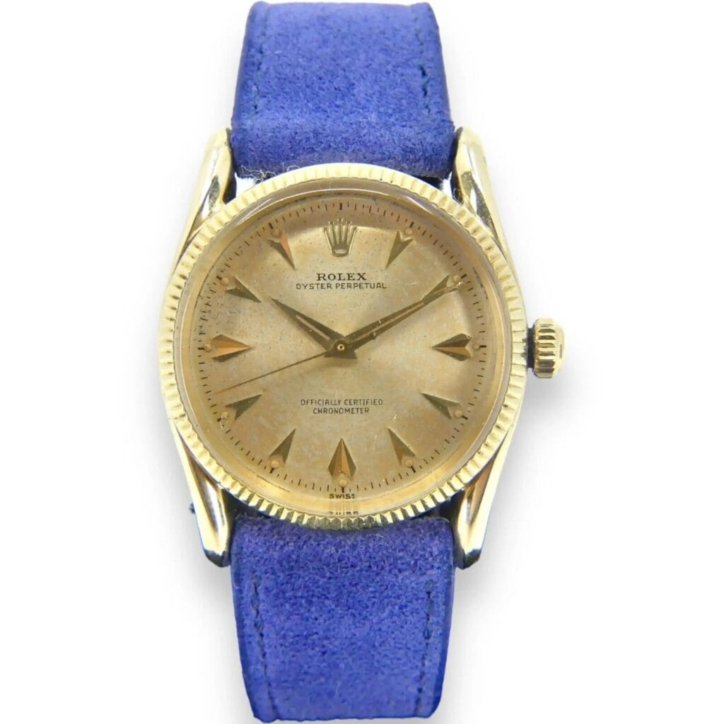 Vintage Rolex 6593 14k Gold Oyster Perpetual with rare Bombay lugs and fluted bezel, featuring a worn dial and blue suede strap, viewed from above on a white background.
