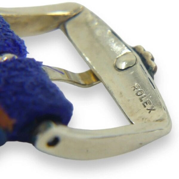 Close-up of a shiny, engraved Rolex clasp on a textured blue strap, featuring the Vintage Rolex 6593 14k Gold Oyster Perpetual with Rare Bombay Lugs & Fluted Bezel against a white background.