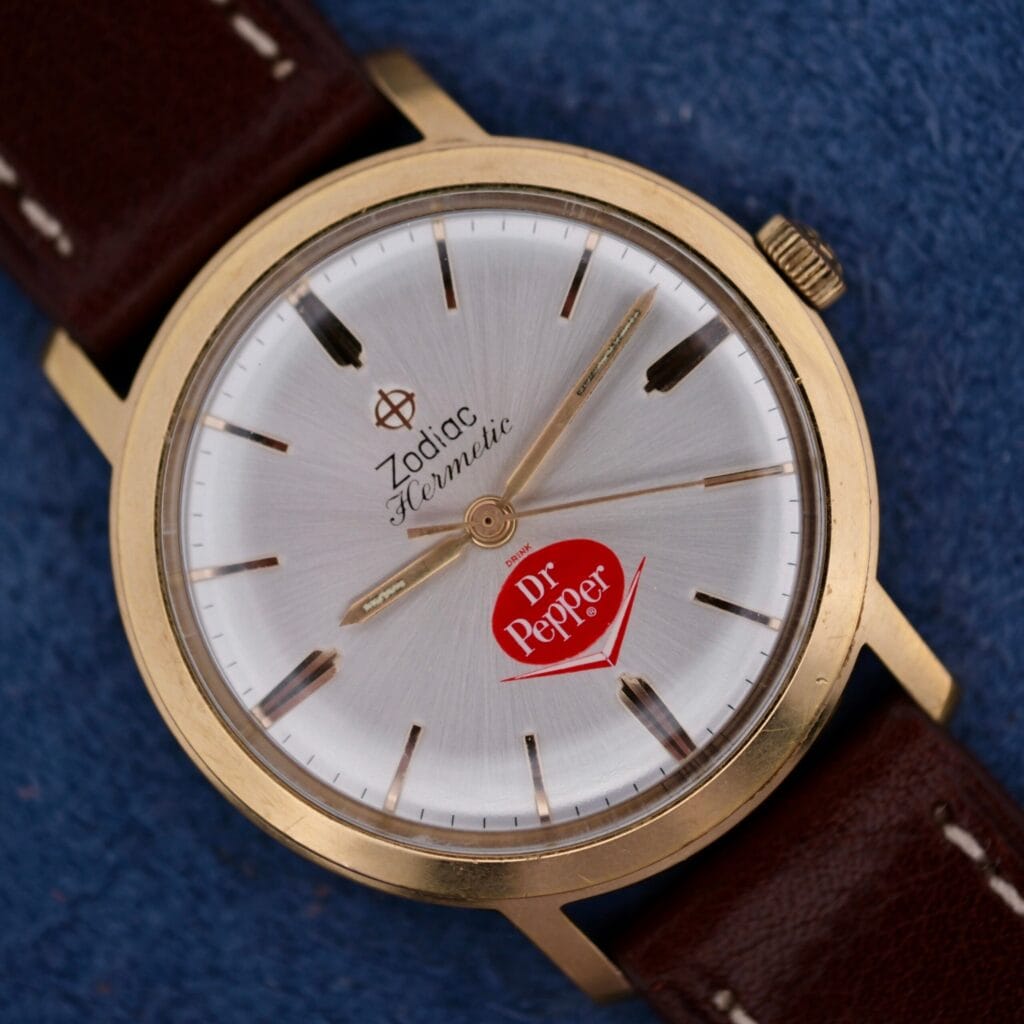 The Zodiac Hermetic 17 Jewels Dr. Pepper Dial features a silver face and a classic brown leather strap, offering vintage style and precision.