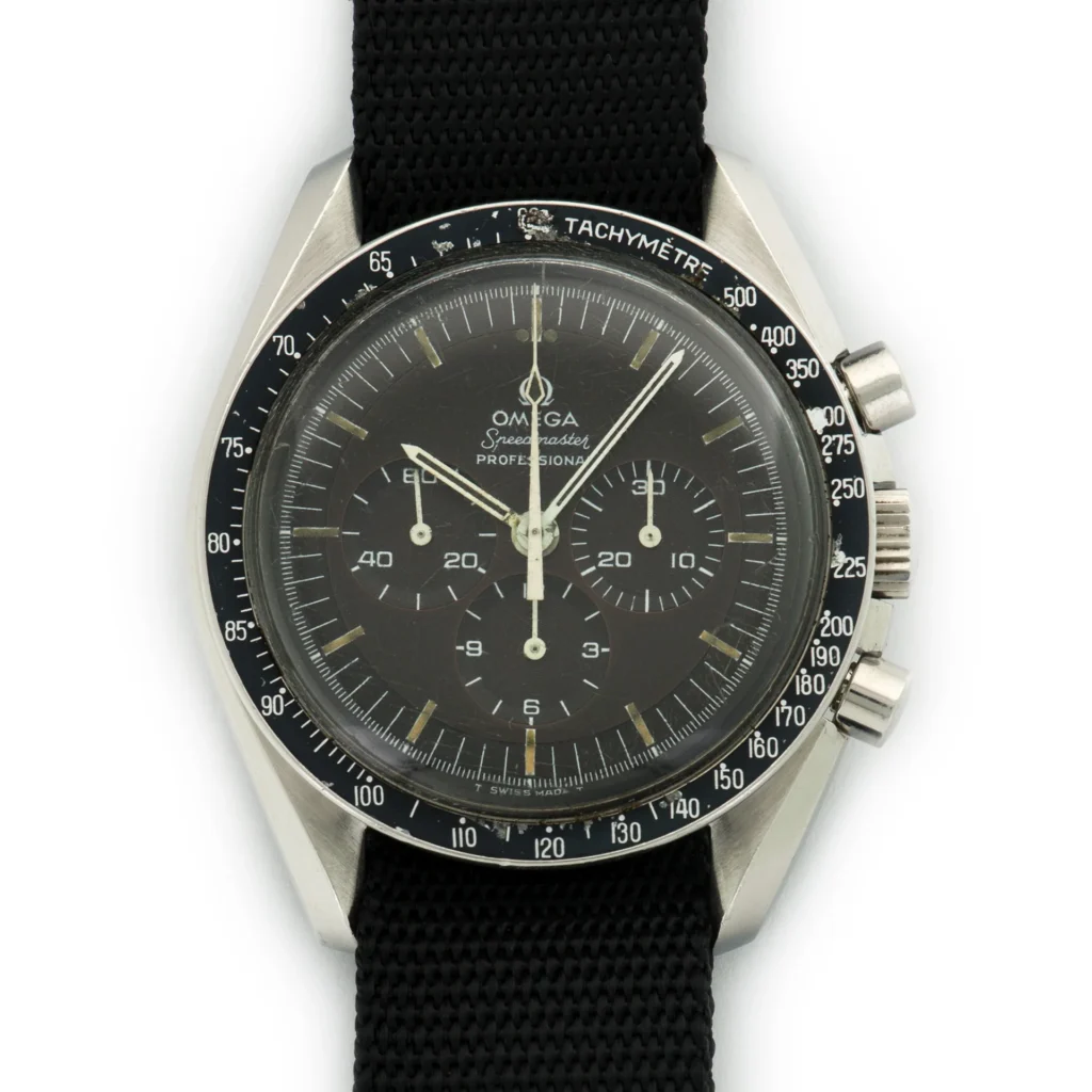 A close-up of an Omega Speedmaster 145.022 Professional wristwatch with a black dial, three subdials, white markers, and a black fabric strap. The tachymeter scale is clearly visible on the bezel.