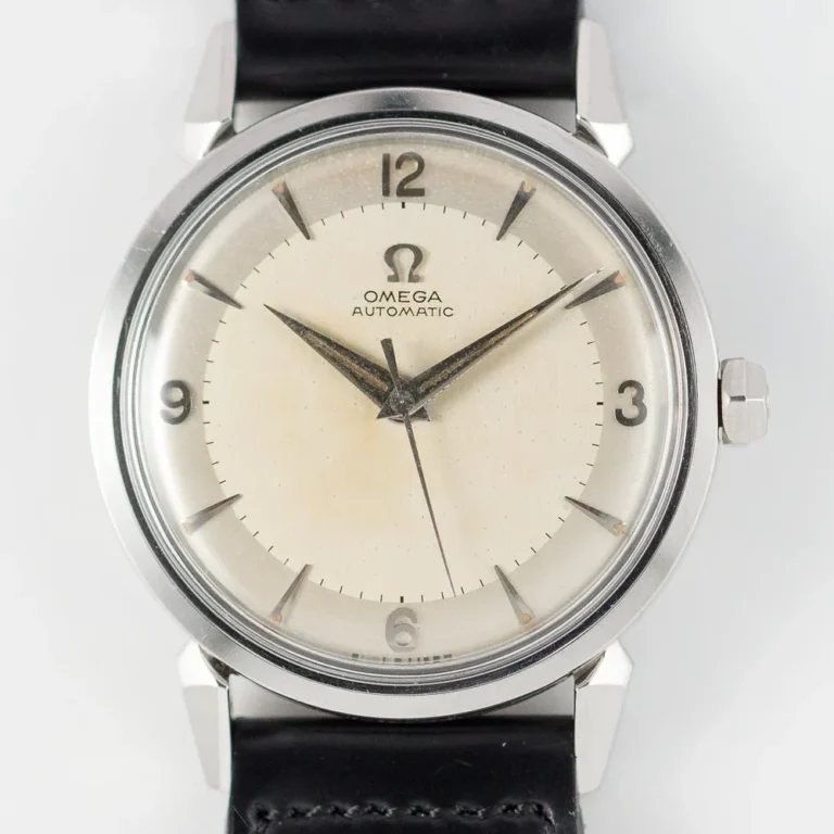 A close-up view of a vintage Omega Seamaster 2832 Automatic wristwatch with a cream-colored dial, silver hour markers, black hands, and a black leather strap. The watch features no date display and minimal branding on the face.
