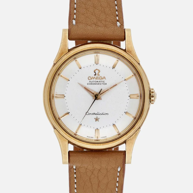 A gold Omega Constellation 14381 automatic chronometer wristwatch featuring a white dial, gold hour markers, and a brown leather strap. The watch face proudly displays the Omega logo and Constellation text.