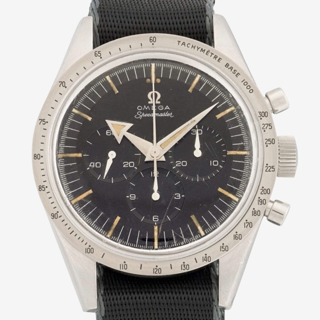 A vintage Omega Speedmaster 2915 wristwatch with a black dial, three subdials, silver hour markers, and a tachymeter scale on the bezel, shown with a black textured strap.