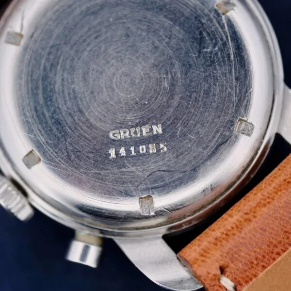 Close-up of a Gruen Chronotimer Steel with Pulsations Dial, showing the back with a scratched stainless steel surface and engraved serial number 141085. It features a round case, side buttons, and is attached to a brown leather strap.