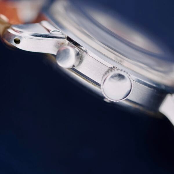 Close-up of the Gruen Chronotimer Steel With Pulsations Dial against a dark background, highlighting the crown and push button on its polished stainless steel case in detailed focus.