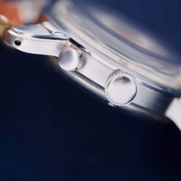 Close-up of the Gruen Chronotimer Steel With Pulsations Dial against a dark background, highlighting the crown and push button on its polished stainless steel case in detailed focus.